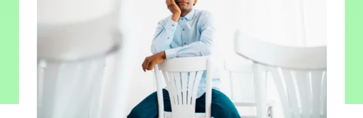 A man sitting in a turned chair giving a speech to an off frame crowd